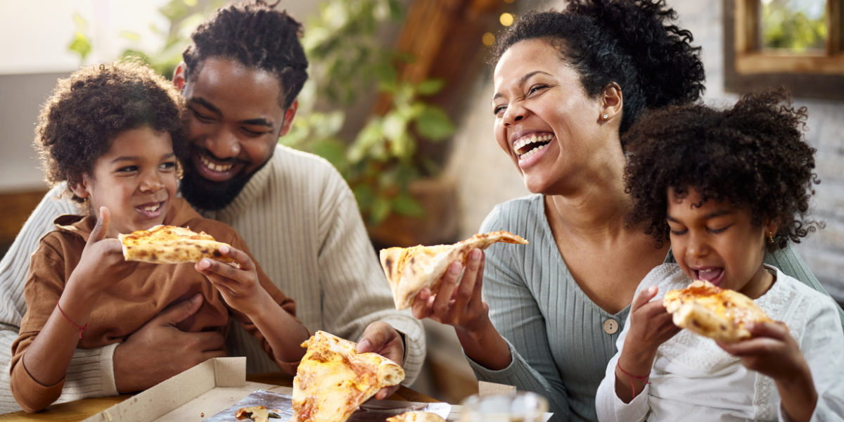 A family laughing as they eat pizza at a restaurant.