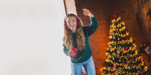 A teen girl excited as she listens to Christmas music. There is a Christmas tree in the background