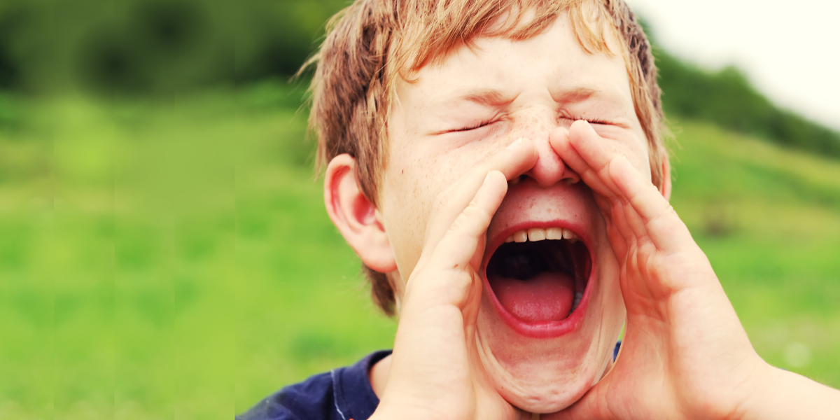 A young boy cupping his hands around his mouth and shouting while he's outside in a field