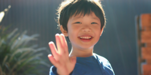 A young asian boy waving at the viewer.