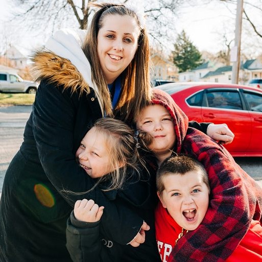 A mom smiling as her happy kids hug her