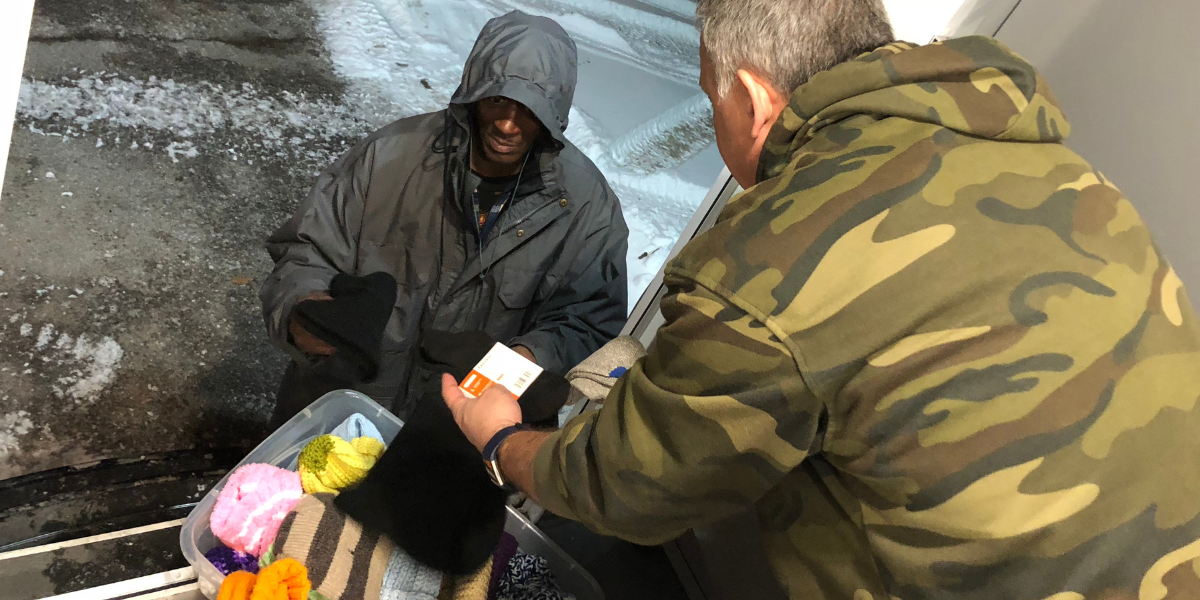 Salvation Army volunteer handing a man who is homeless some warm winter items