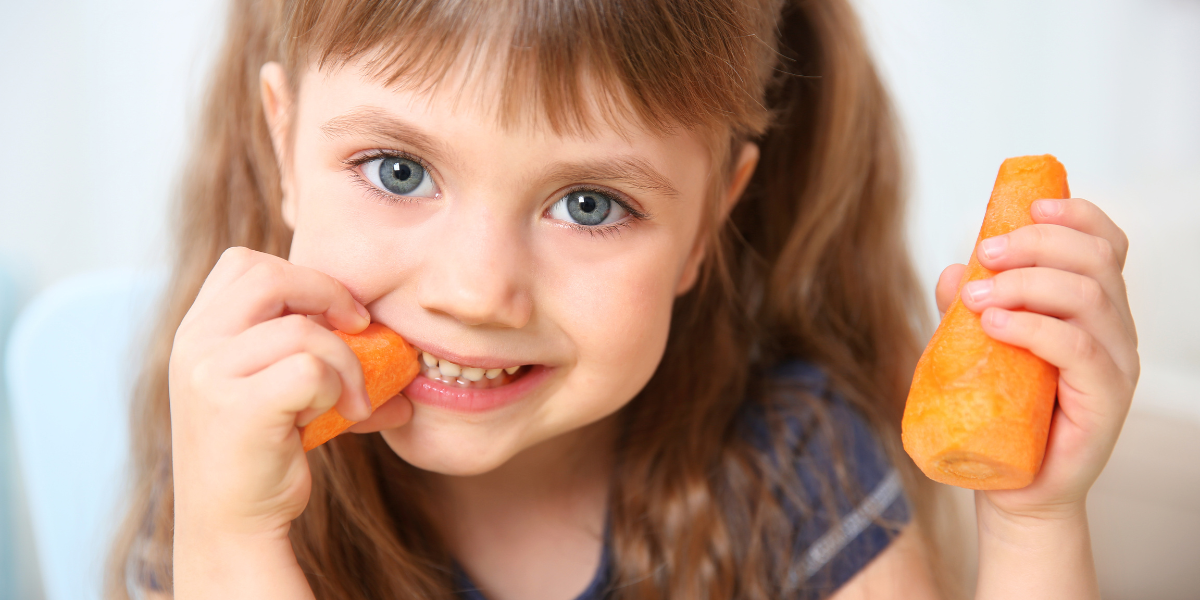 A little girl eating a carrot and smiling